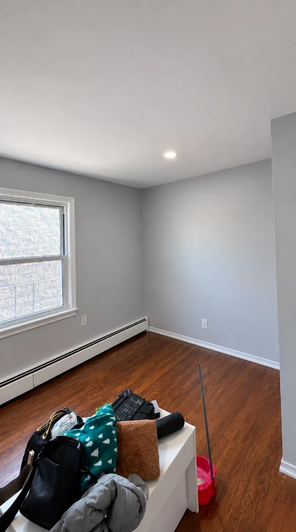 Apartment bedroom with smooth cool light gray walls, a white ceiling with a recessed light, crisp white window trim and baseboards, and hardwood floors