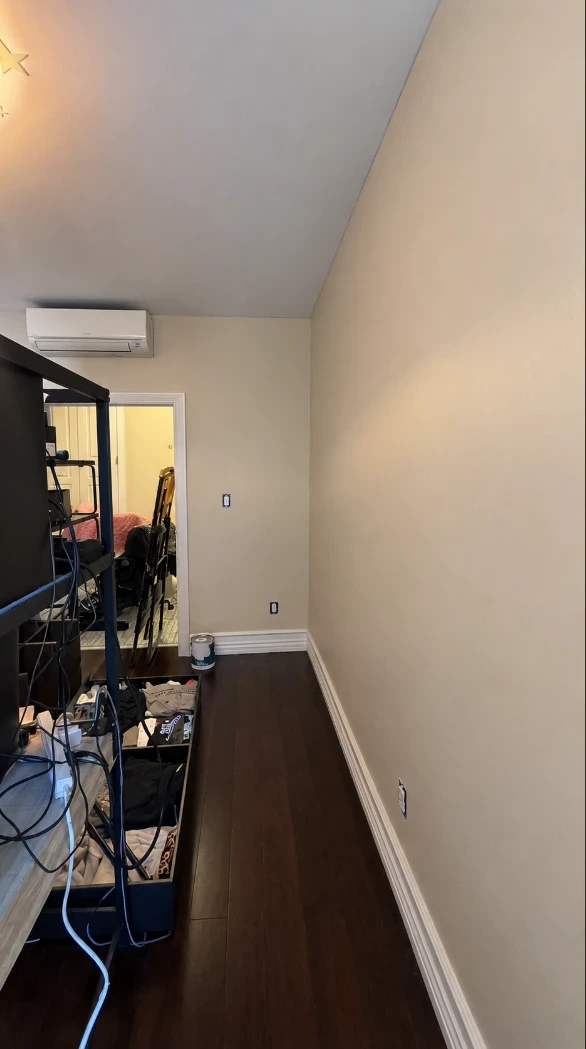 Apartment bedroom with warm taupe walls, white baseboards, a wall-mounted air conditioner and a doorway to the next room