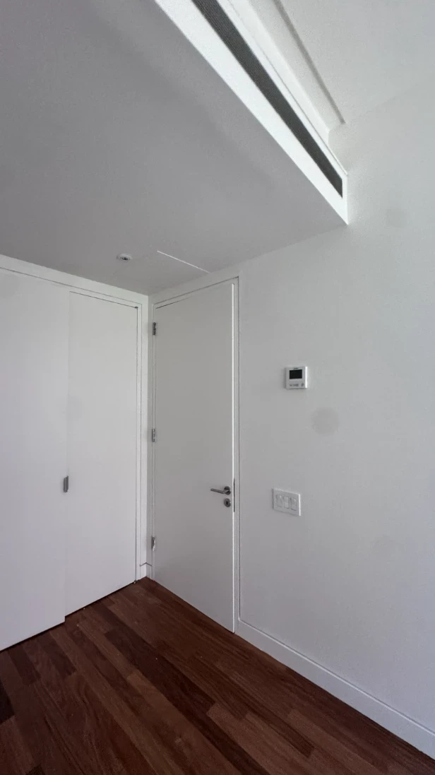 Apartment bedroom with smooth white walls and ceiling, a flat white door with a lever handle, white closet doors and hardwood floors