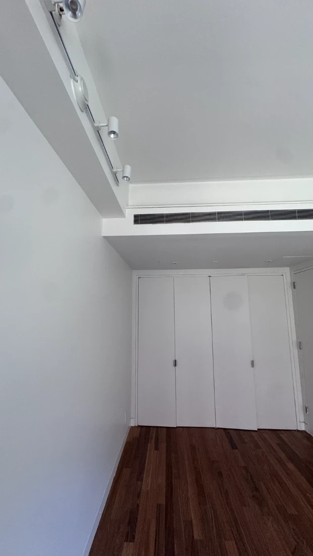 Apartment bedroom corner with smooth white walls, a ceiling track light, a linear ceiling vent, white folding closet doors and dark hardwood floors