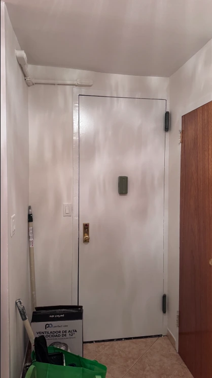 The same apartment entry hall after painting, with clean white walls, ceiling, exposed pipe and front door