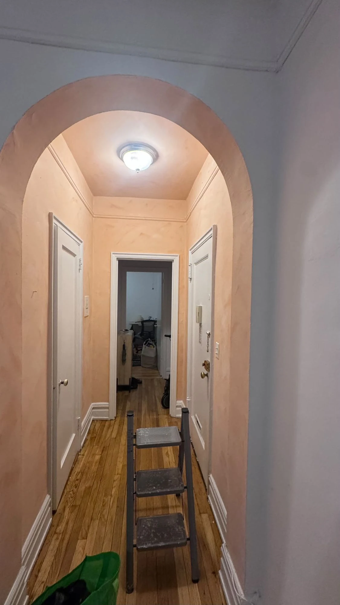 Arched apartment hallway finished in soft peach lime wash on the walls, arch and ceiling, with white doors and trim and hardwood floors
