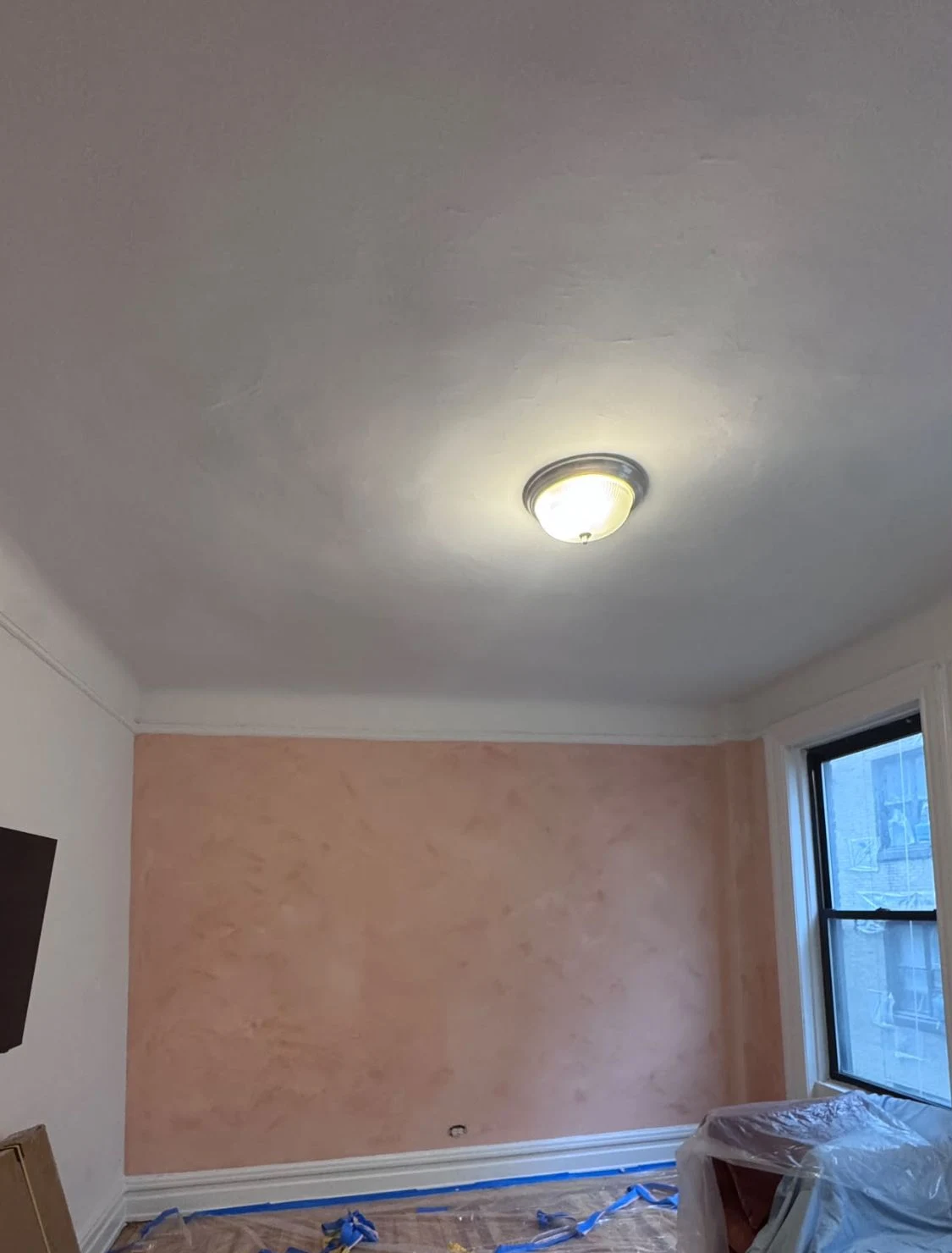 Apartment room with a lime wash wall in dusty pink, with the floor covered in plastic sheeting and blue tape along the baseboard