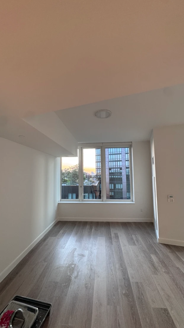 Empty apartment living room freshly painted in clean white on the walls, ceiling and baseboards, with large windows and gray wood-look floors