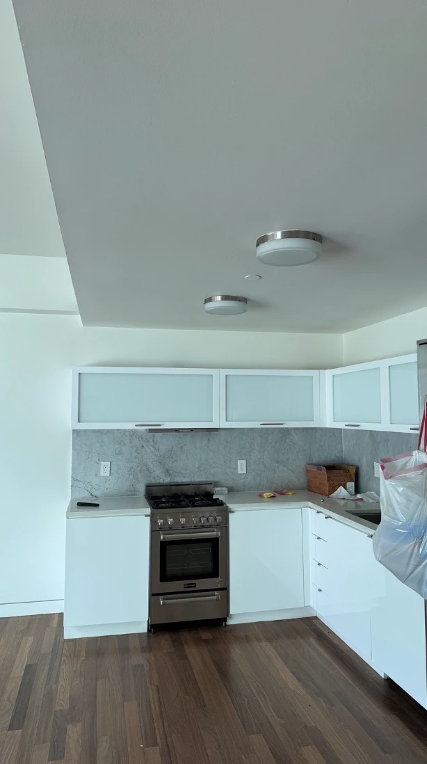 Apartment kitchen with white walls and ceiling, white cabinets with frosted glass doors, a stone backsplash, a stainless steel range and dark hardwood floors