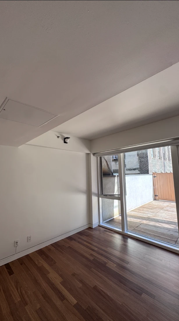 Apartment living area with clean white walls and ceiling, dark hardwood floors and a floor-to-ceiling glass door that opens onto a wood deck