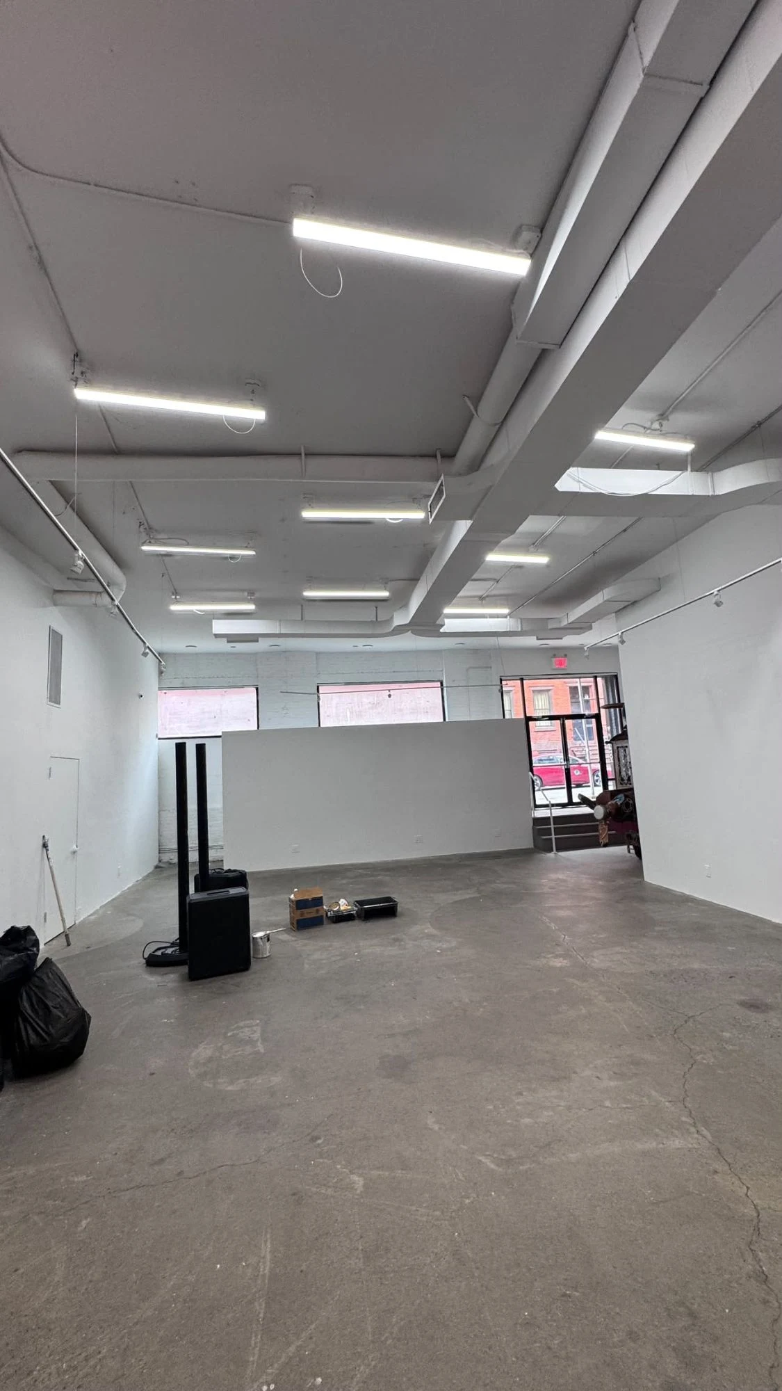 Wide view of a large commercial space with smooth white walls, a white open ceiling with ducts and track lighting, a concrete floor and a glass entrance door