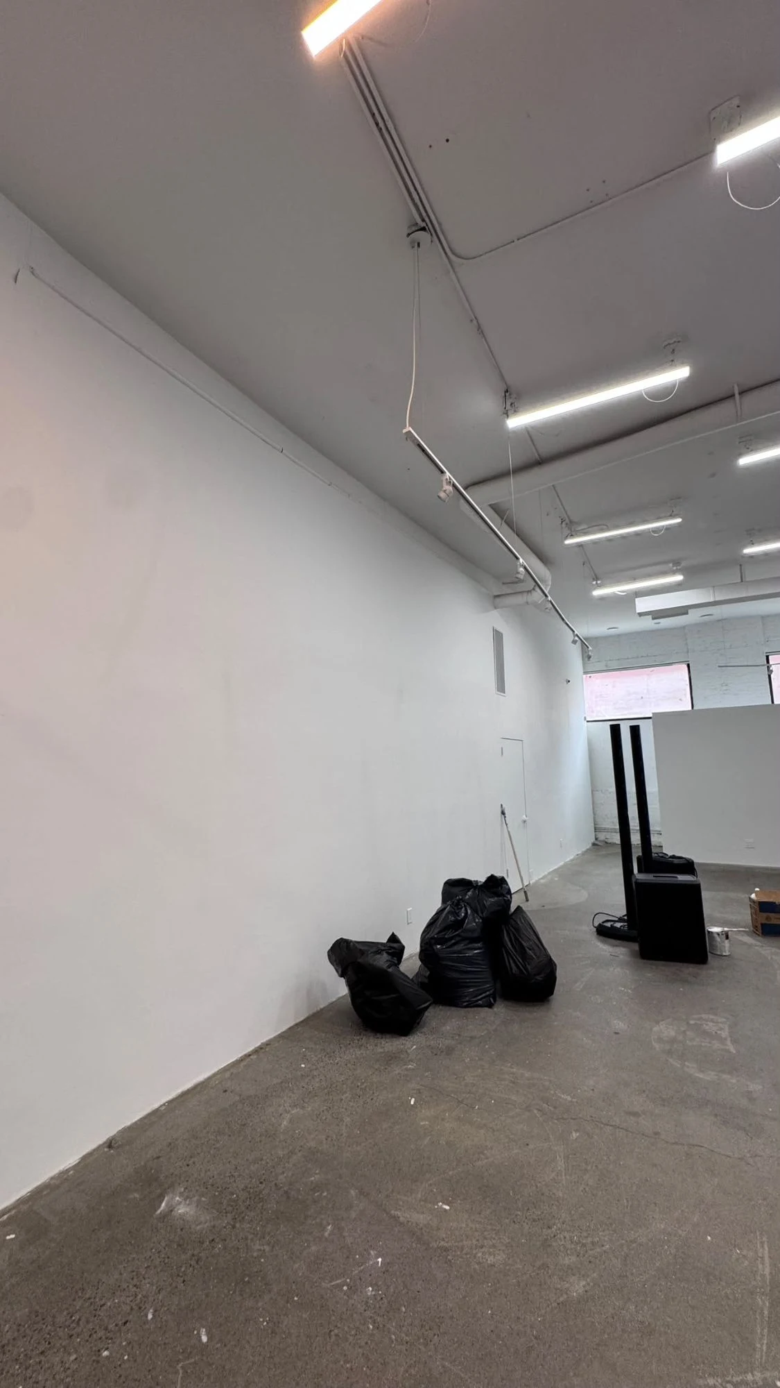 Large commercial space with tall, smooth white walls, an open ceiling with white ducts and pipes, track lighting and a concrete floor