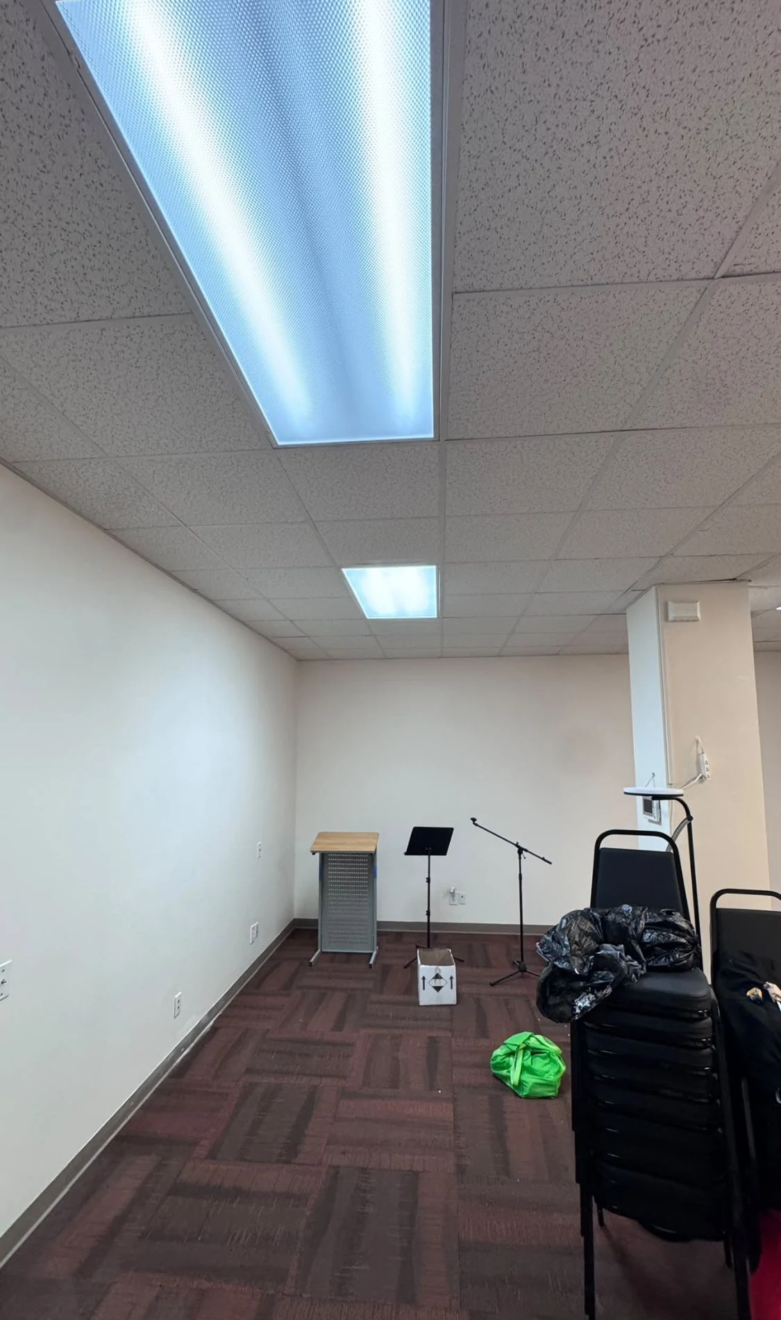 Commercial meeting room with fresh warm white walls, a podium and a microphone stand against the far wall, and dark carpet tiles